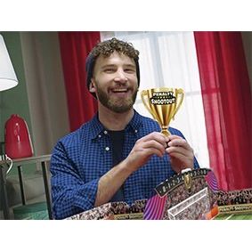 Mężczyzna cieszący się trzymając puchar nagrody za wygraną w grę piłkarską karniaki w domu