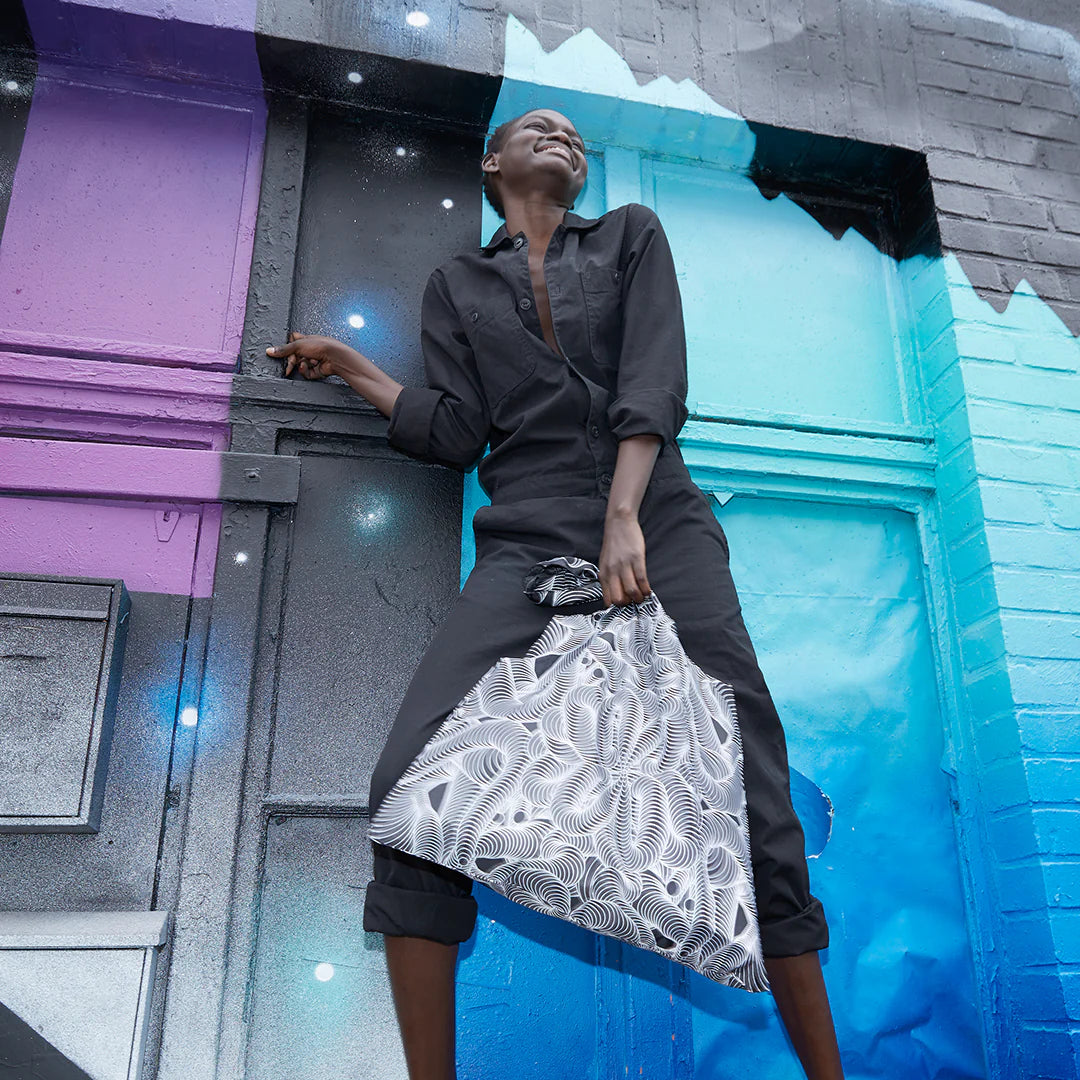 Torba podręczna wzorzysta w czarno białe wzory noszona przez kobietę na tle kolorowej ściany graffiti