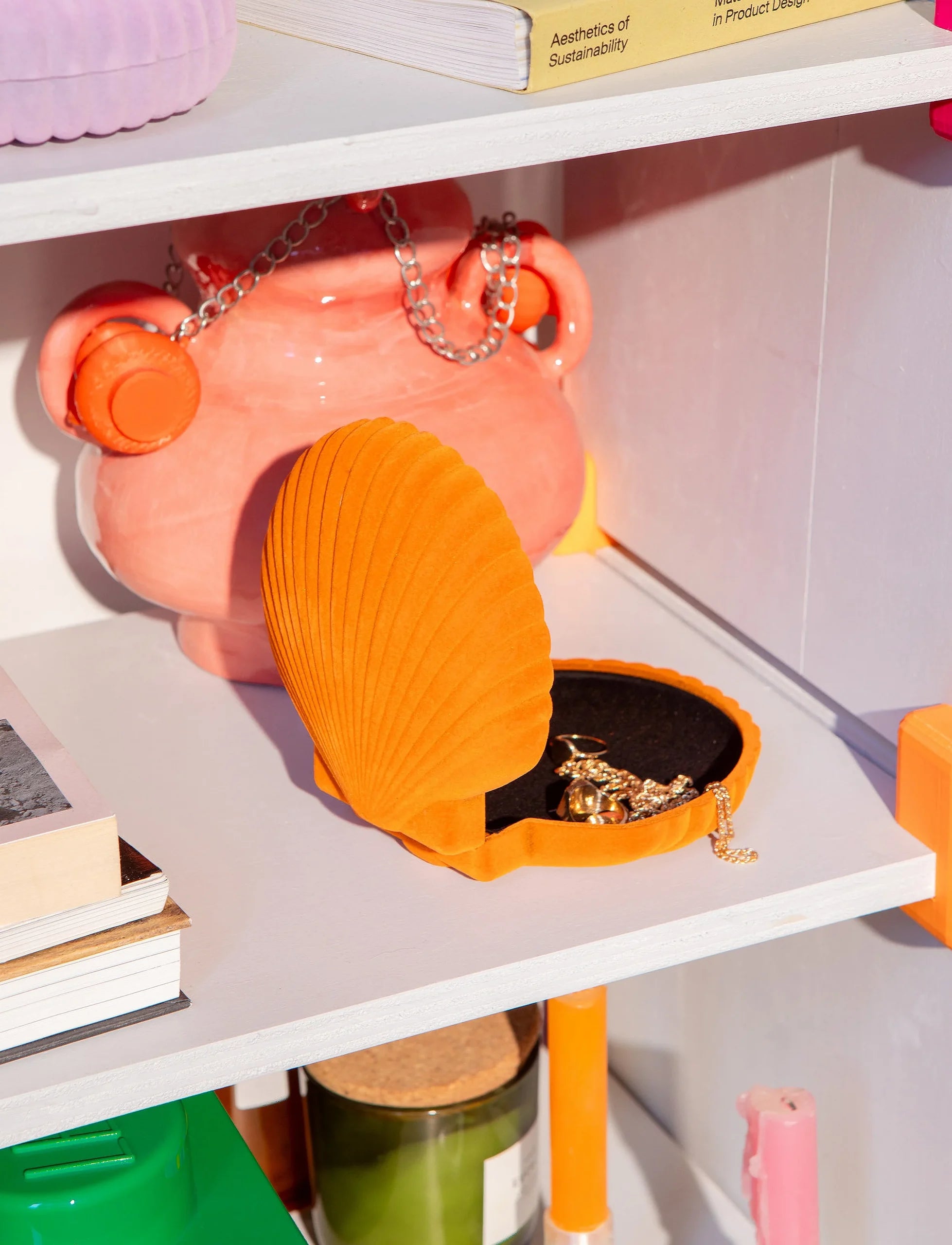 Pomarańczowa szkatułka Venus pomarańczowa w kształcie muszli na białej półce z biżuterią