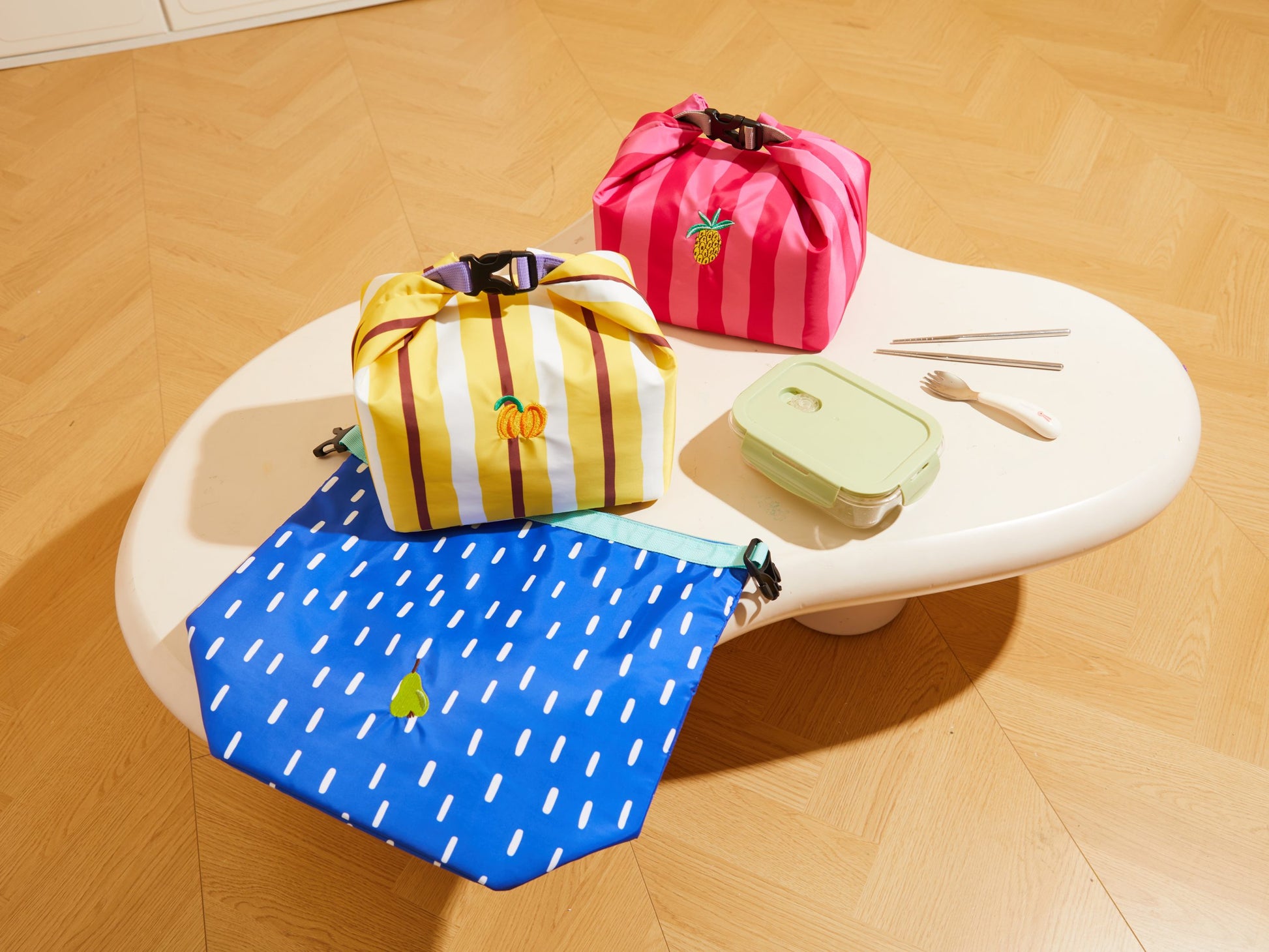 Kolorowa torba na lunch pineapple party marki MOB o wzorze pasków i owoców na stole