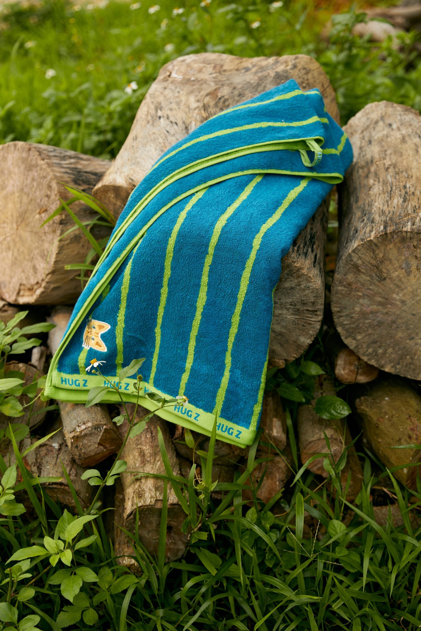 Ręcznik kąpielowy dla dzieci Mideer w niebiesko-zielone paski na drewnianych kłodach na zewnątrz