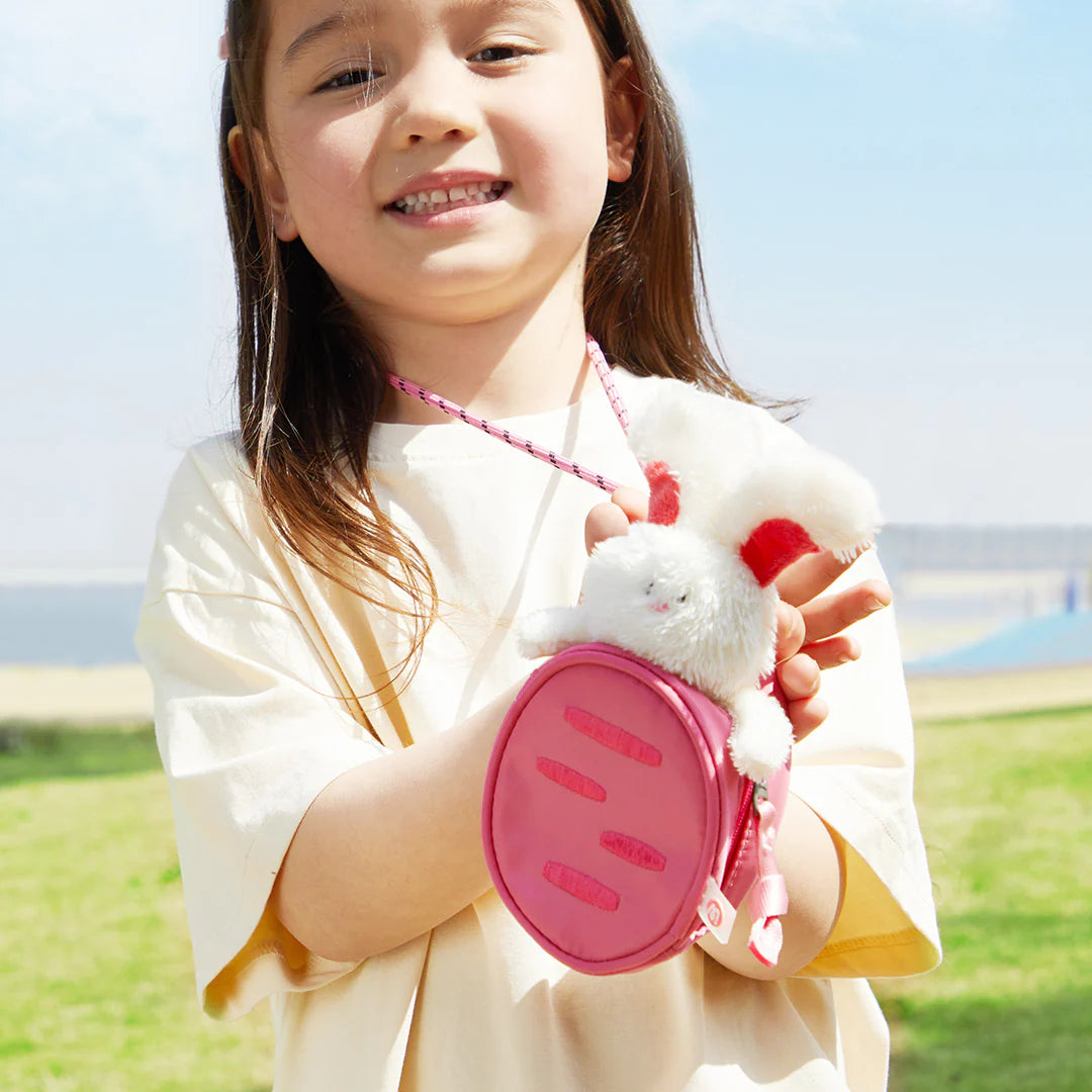 Mały plecak dla dzieci króliczek marki mideer w różowym kolorze trzymany przez uśmiechniętą dziewczynkę na zewnątrz