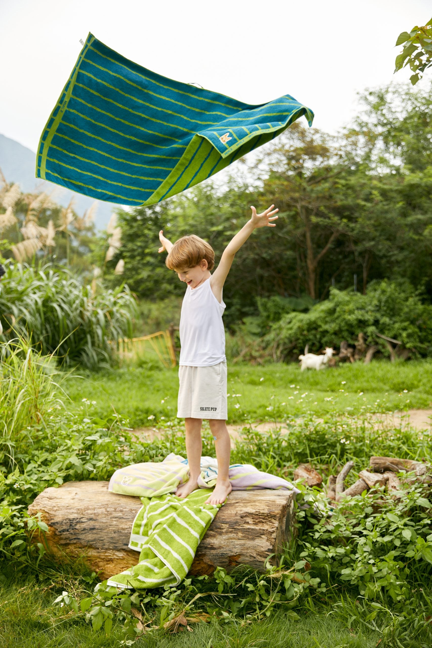 Chłopiec bawiący się na tle zieleni z niebiesko-zielonym ręcznikiem kąpielowym dla dzieci Mideer
