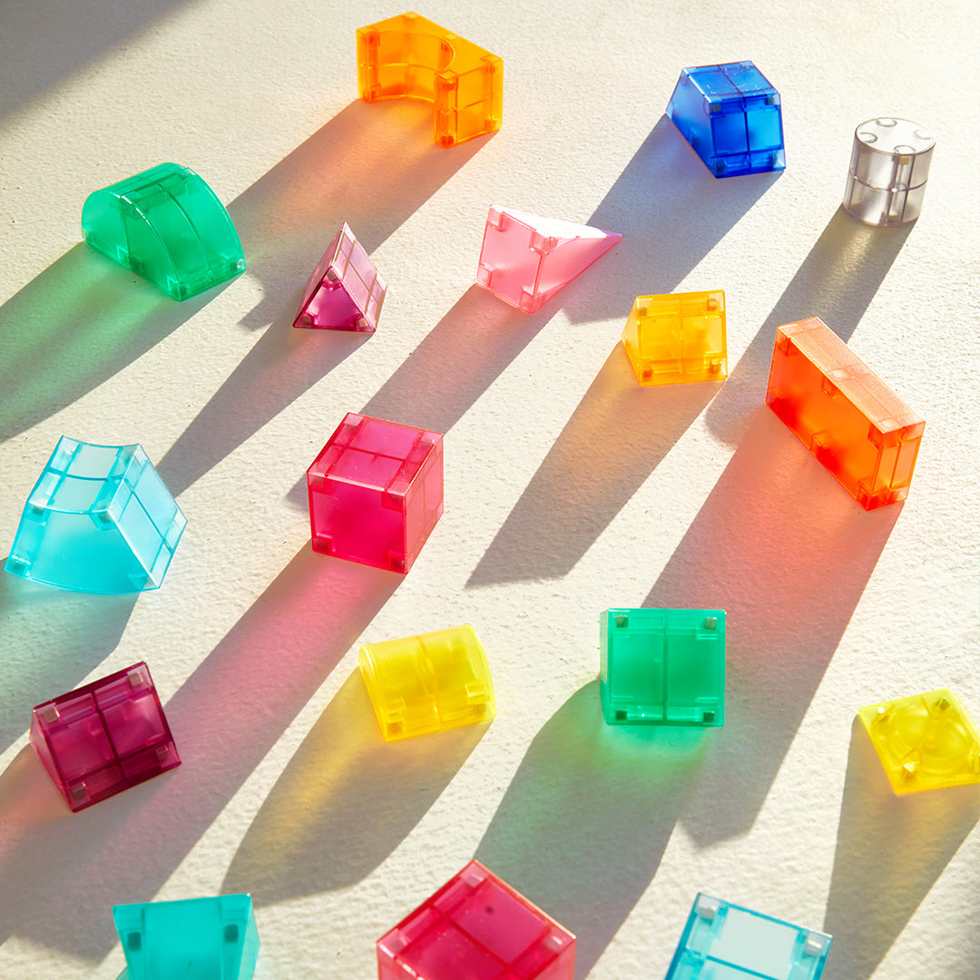 Kolorowe klocki magnetyczne 3D w różnych kształtach ułożone na jasnej powierzchni z cieniami