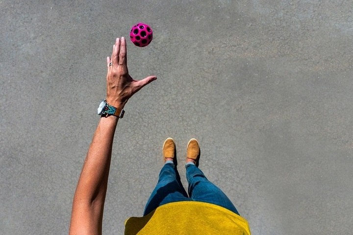 Osoba rzucająca różową piłeczką Waboba Moon Ball żółta na szarym tle z góry