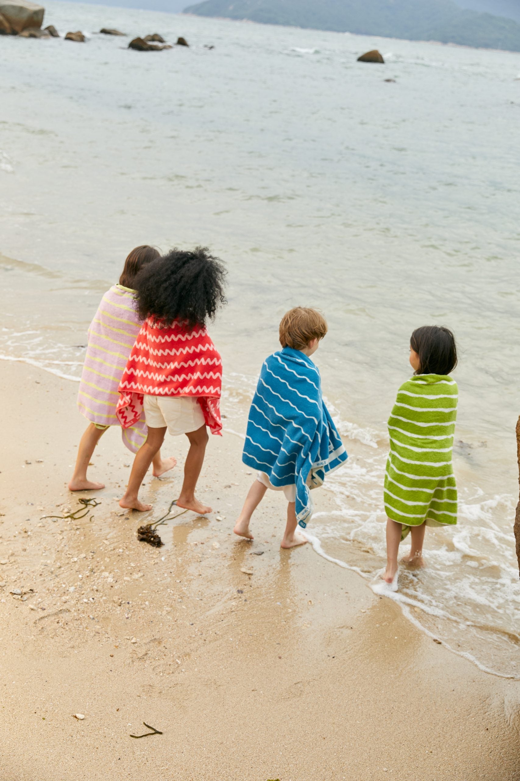Dzieci na plaży owinięte ręcznikami kąpielowymi, w tym różowy ręcznik kąpielowy dla dzieci różowy