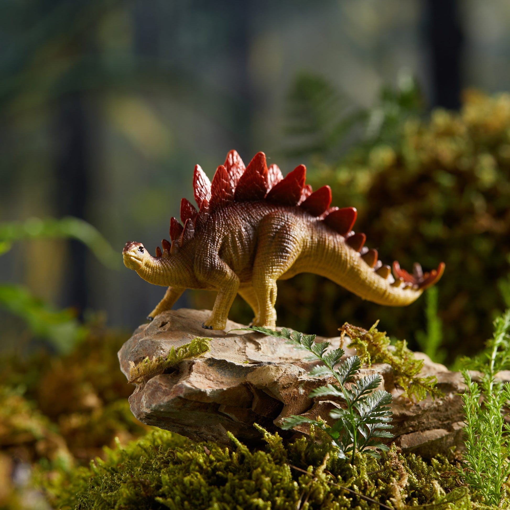 Zestaw figurek dinozaurów dla dzieci przedstawiający realistyczną figurkę stegozaura na tle zielonej roślinności