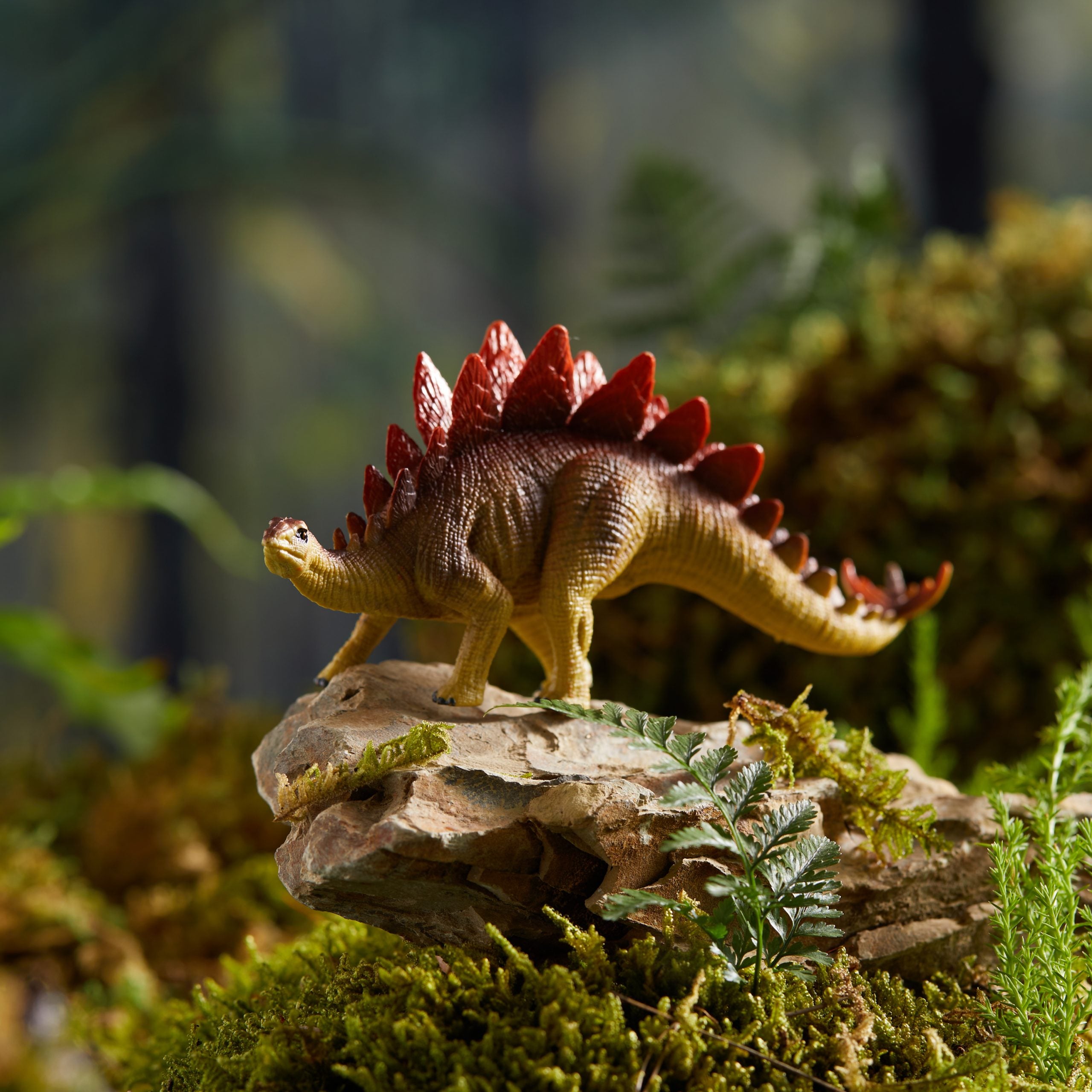 Zestaw figurek dinozaurów dla dzieci przedstawiający realistyczną figurkę stegozaura na tle zielonej roślinności