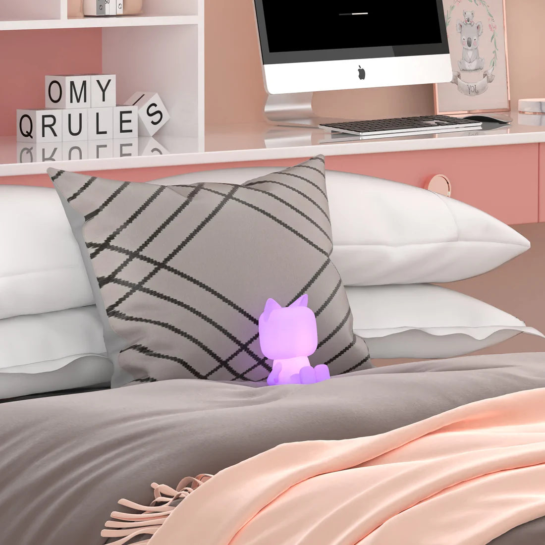 Lampka nocna kot świecąca na fioletowo ustawiona na łóżku z szarą poduszką i różowym kocem
