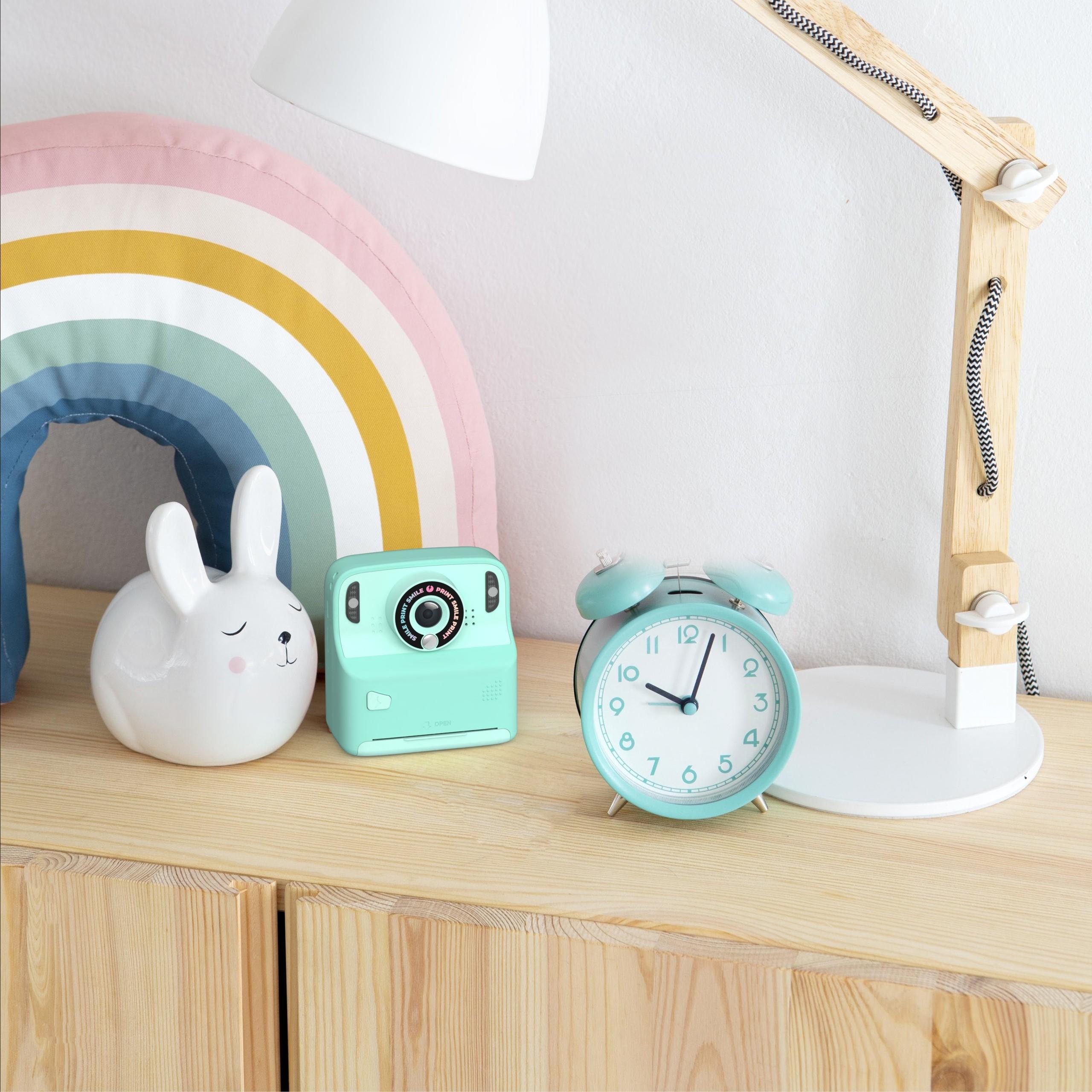 Miętowy aparat cyfrowy z funkcją drukowania obok budzika i lampki na drewnianym blacie