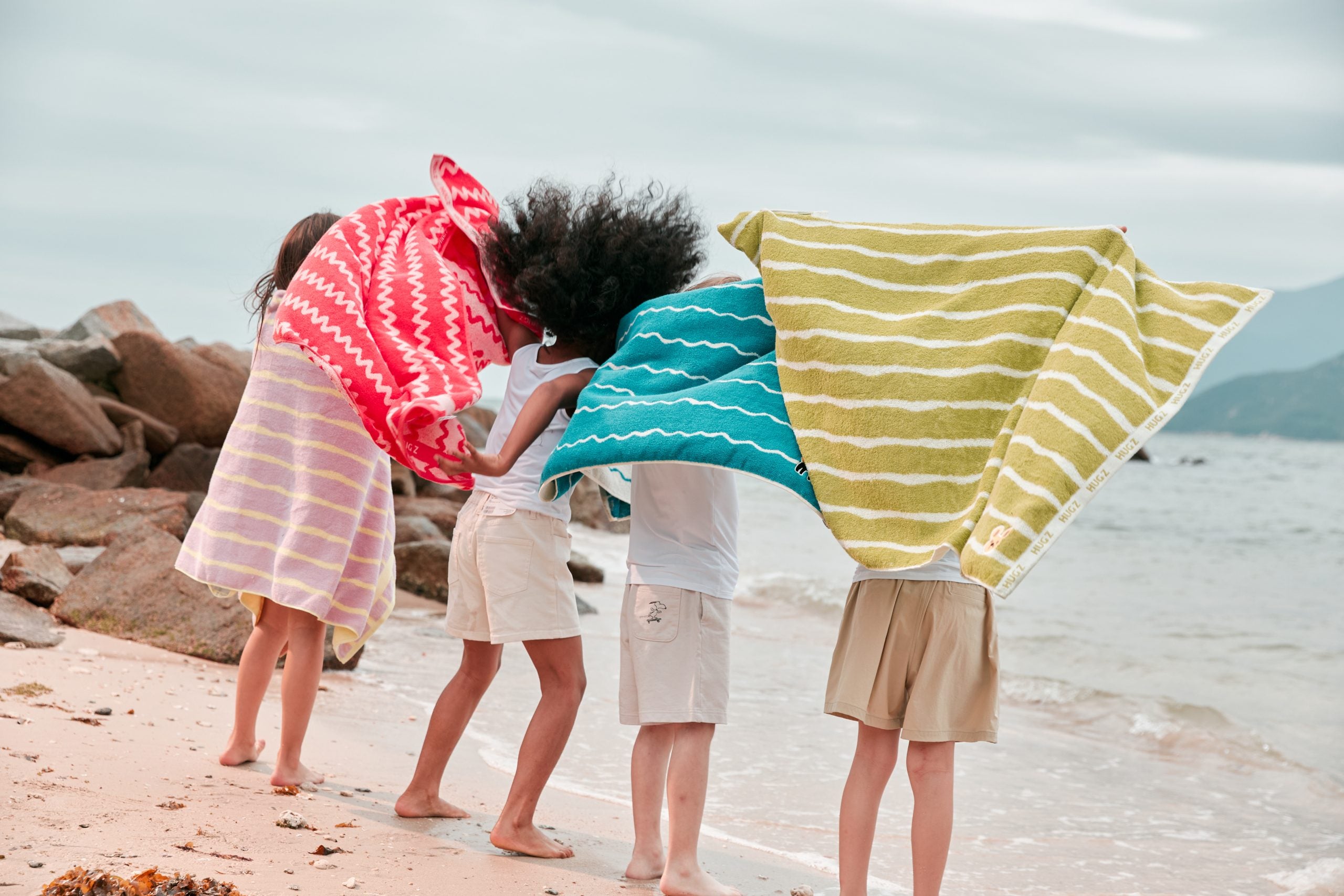 Dzieci na plaży z ręcznikami kąpielowymi w różnych kolorach w tym ręcznik kąpielowy dla dzieci różowy