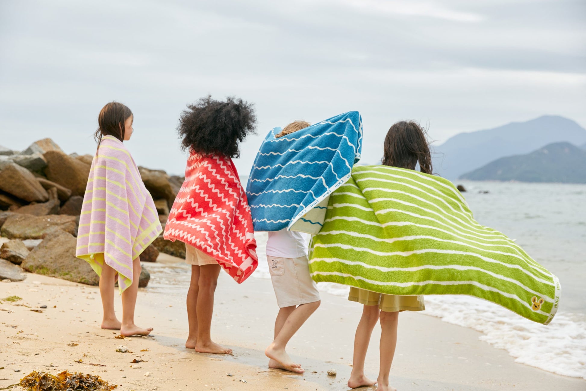 Cztery dzieci owinięte kolorowymi ręcznikami kąpielowymi na plaży jedna z nich ma różowy ręcznik kąpielowy dla dzieci różowy