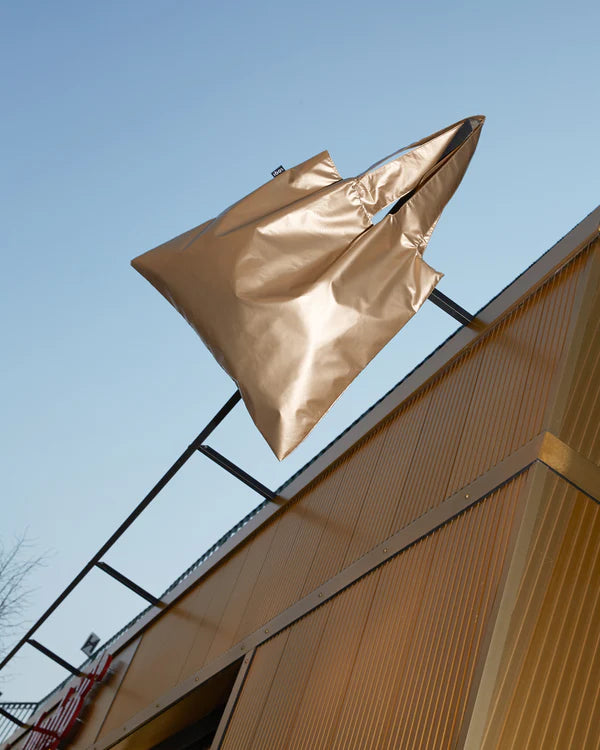 torba LOQI złota z błyszczącego materiału zawieszona na metalowej konstrukcji na tle nieba