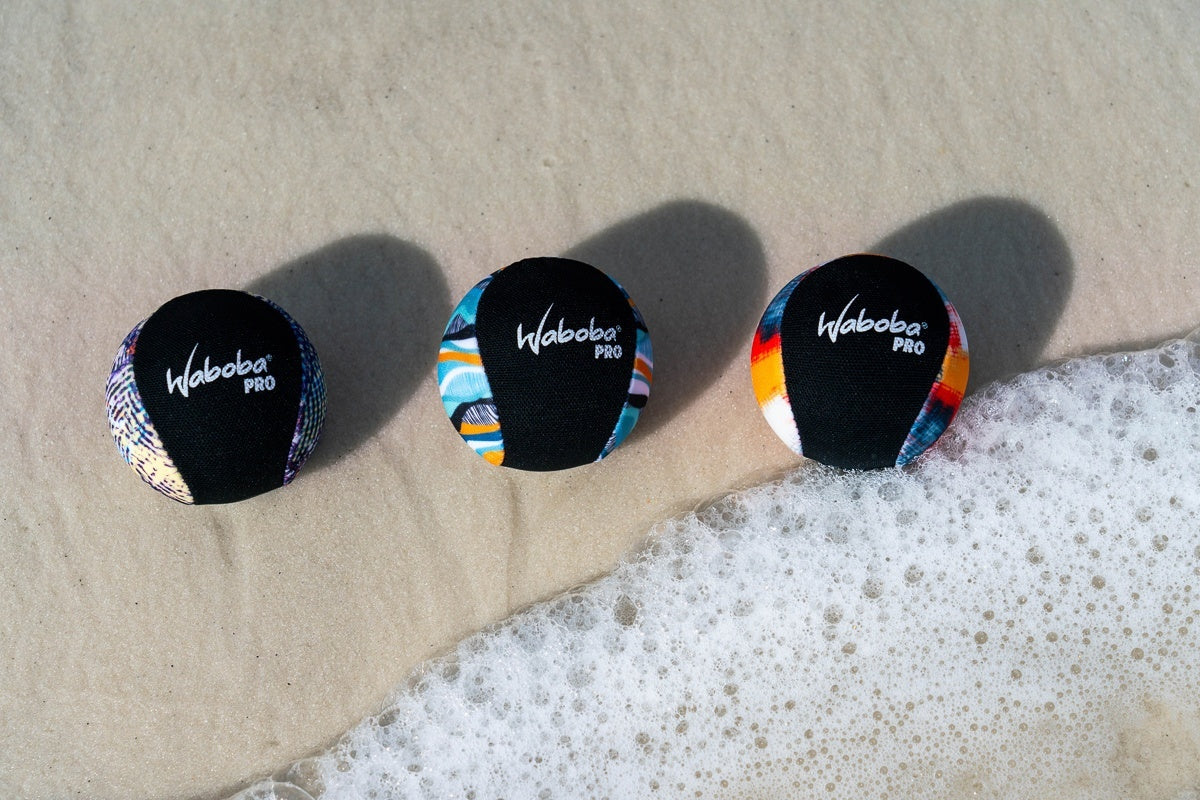 Trzy kolorowe piłeczki Waboba Pro do odbijania na wodzie leżące na piasku przy brzegu morza