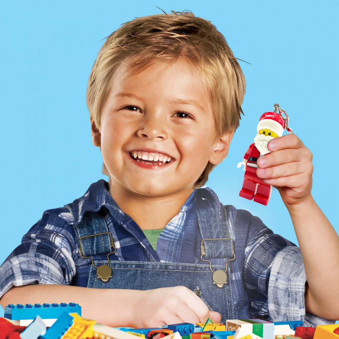 Uśmiechnięty chłopiec trzyma brelok z latarką LEGO Mikołaj w czerwonym stroju świątecznym