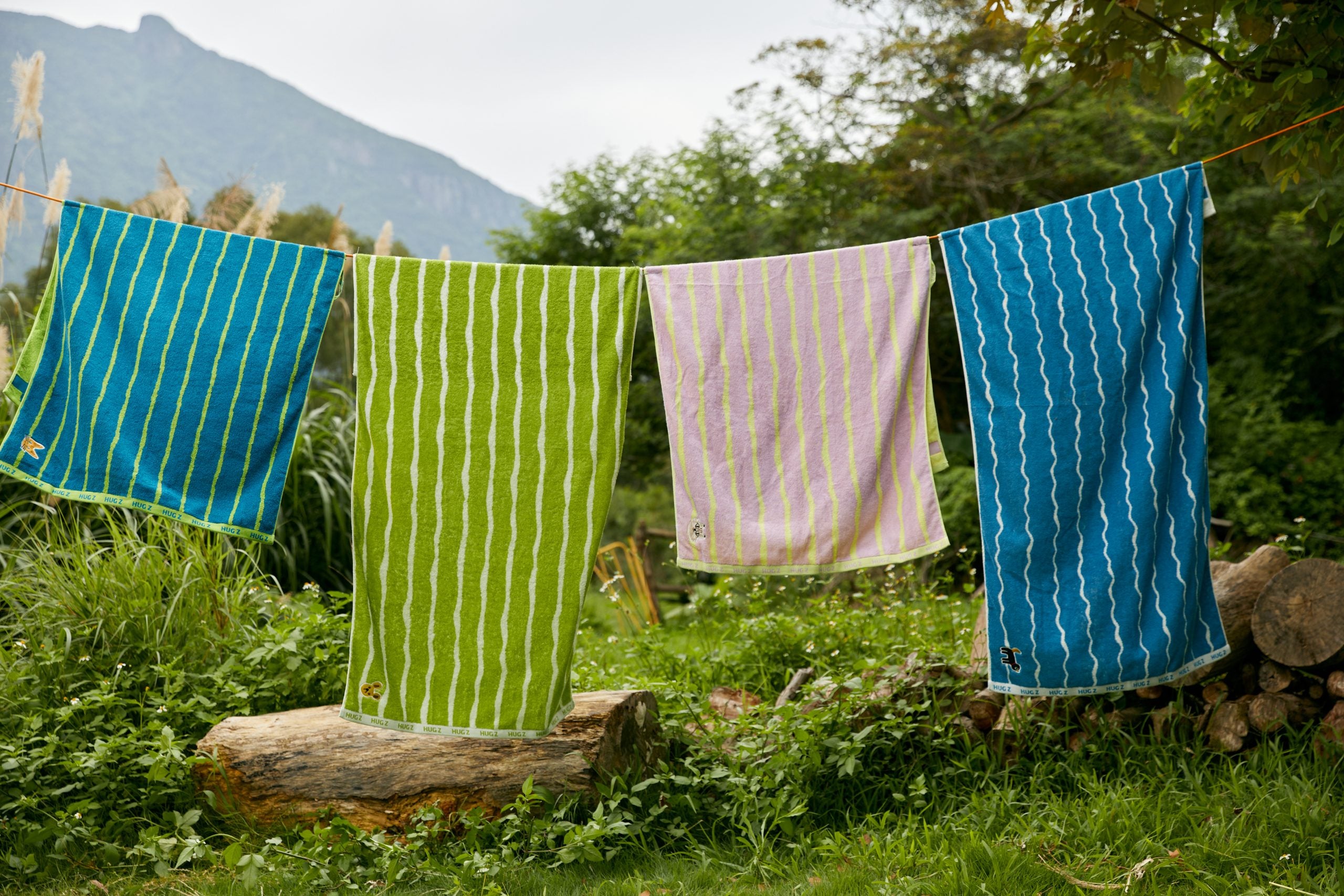 Ręcznik kąpielowy dla dzieci Mideer w różnych kolorach wiszący na sznurku na tle zieleni i gór