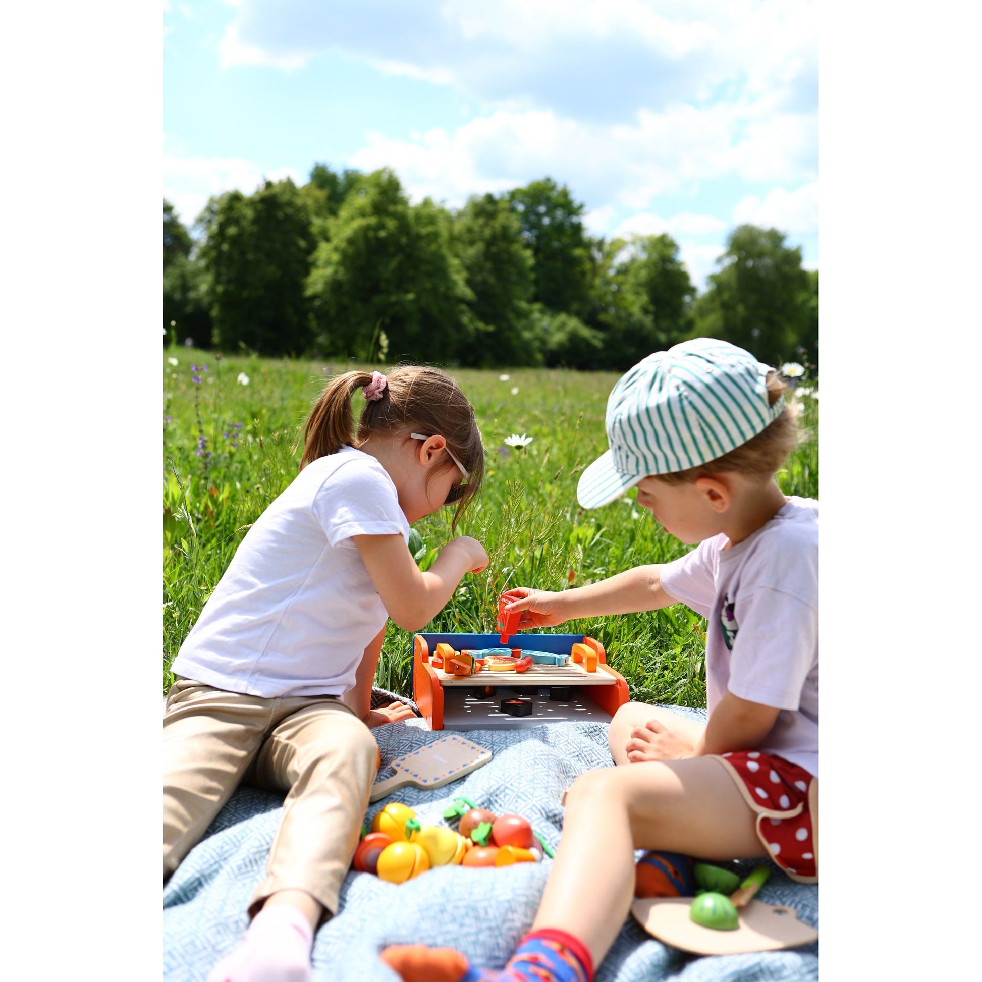 Dzieci bawiące się drewnianym grillem dla dzieci na kocu na świeżym powietrzu