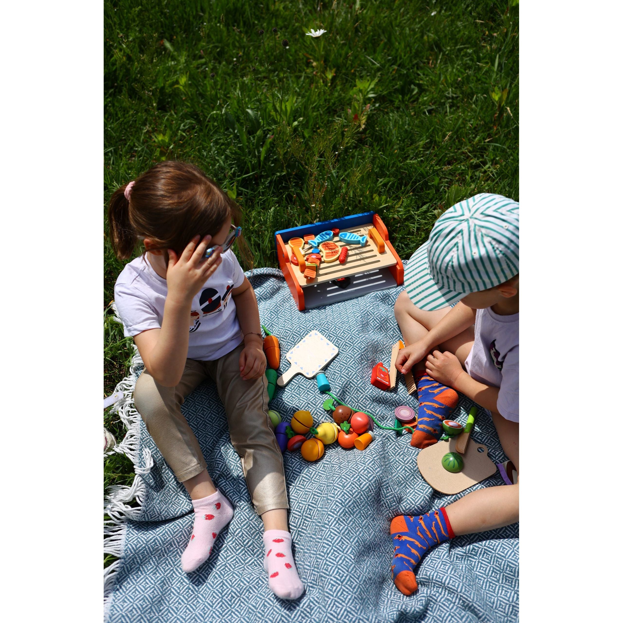 Dzieci bawiące się drewnianym grillem dla dzieci marki MOB podczas pikniku na trawie