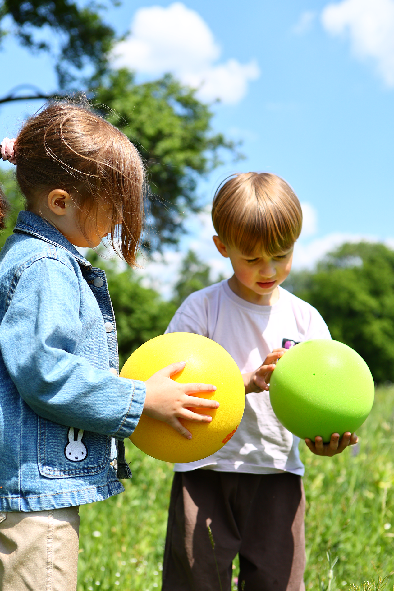 Dwoje dzieci bawiących się na zewnątrz z kolorowymi cichymi puszystymi piłkami w zielonym parku