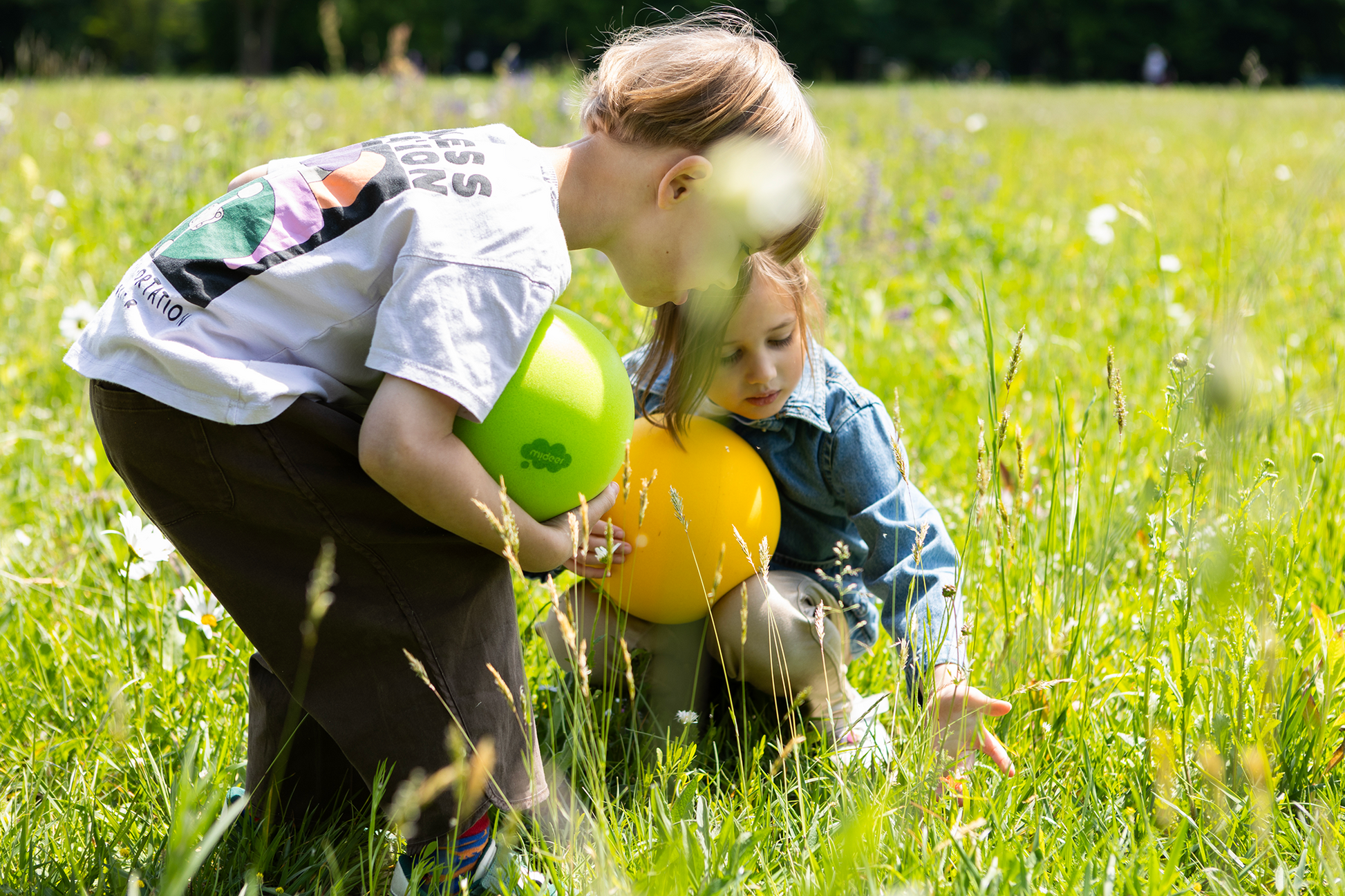Dzieci bawiące się na łące z cichą puszystą piłką w zielonym i żółtym kolorze