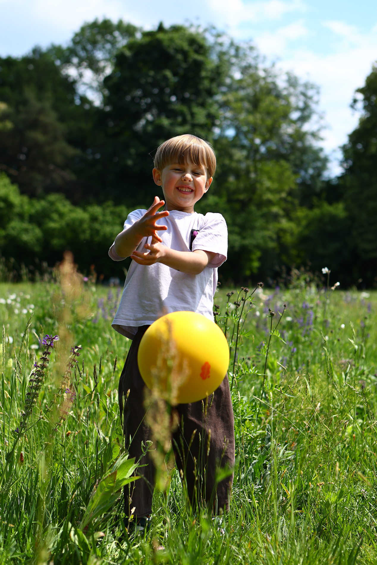 Dziecko bawiące się żółtą cichą piłką dla dzieci na tle zielonej łąki i drzew