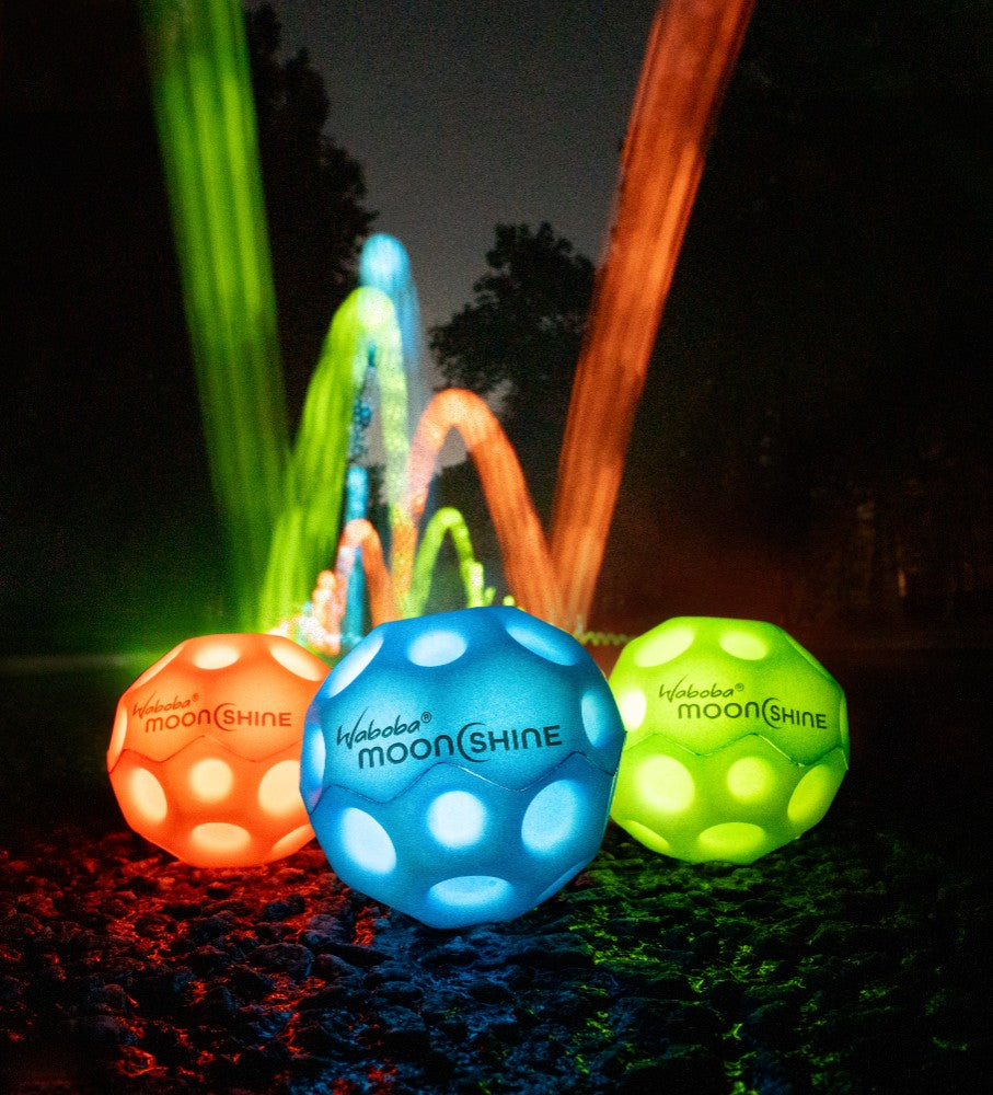 Niebieska piłeczka Waboba Moonshine niebieska świecąca na ciemnym tle z kolorowymi światłami