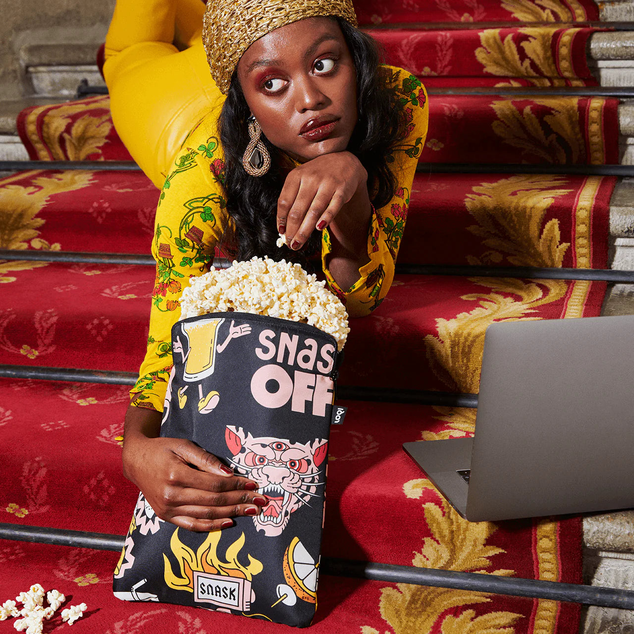 Torba na laptopa LOQI z kolorowym nadrukiem trzymana przez kobietę na czerwonych schodach obok laptopa