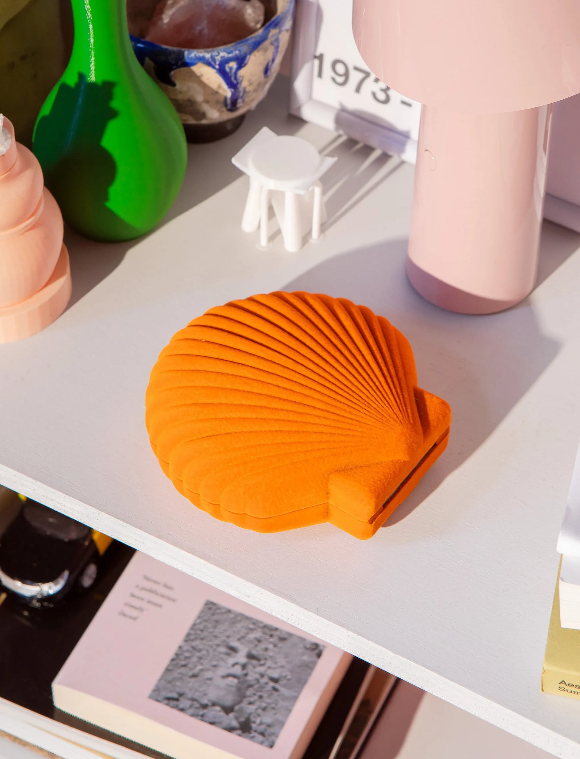 Pomarańczowa szkatułka Venus pomarańczowa w kształcie muszli na białej półce z dekoracjami