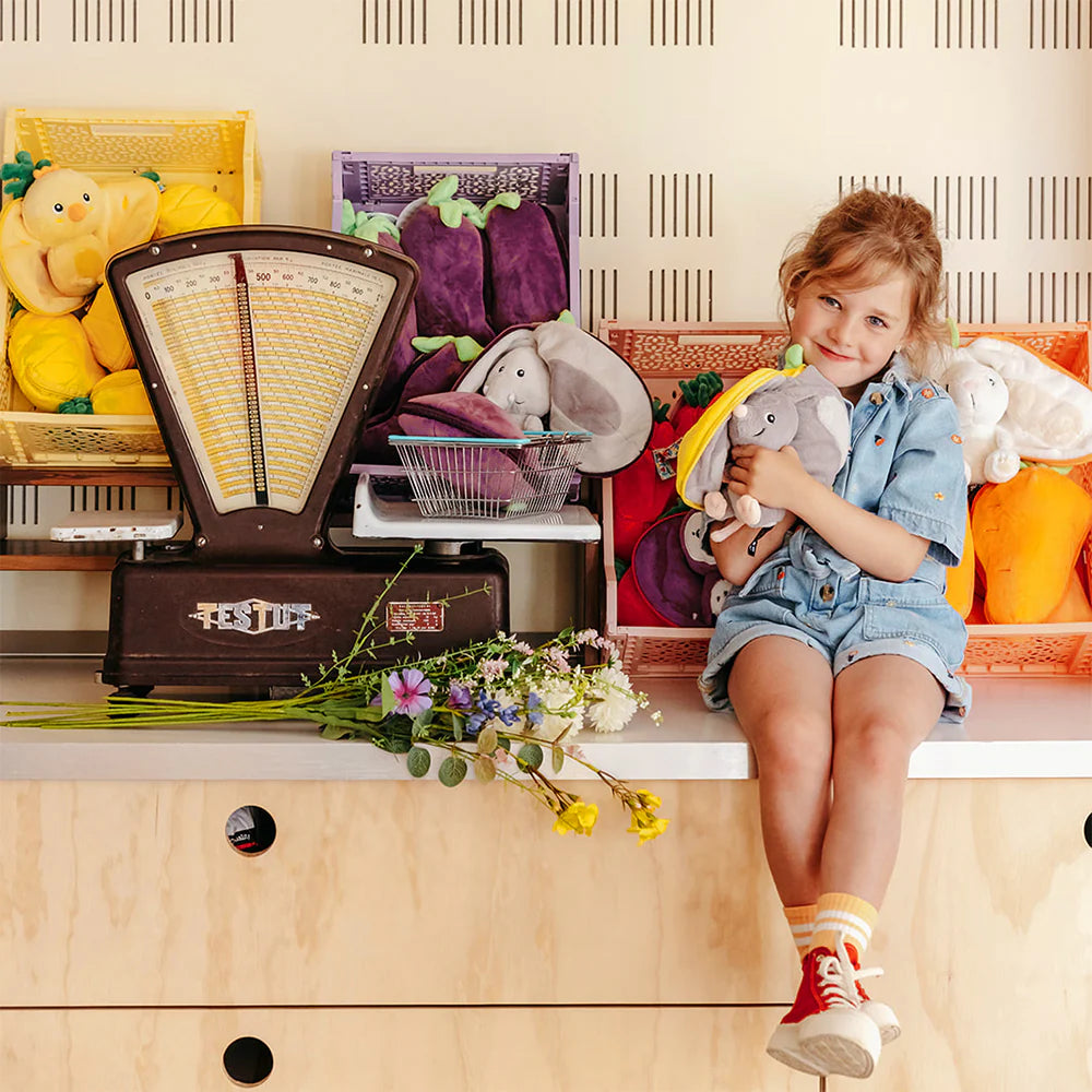 Dziecko trzymające pluszową myszkę w cytrynie siedząc obok kolorowych pluszowych warzyw i starej wagi