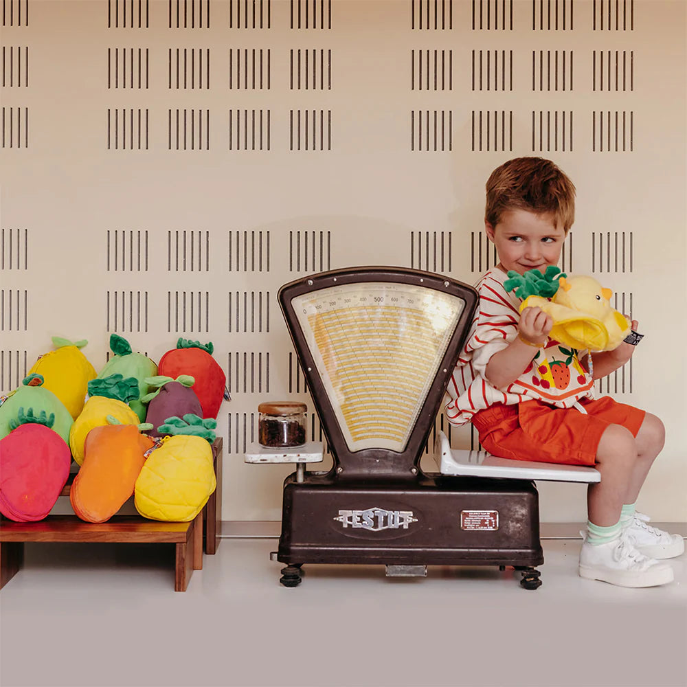 Pluszak kurczaczek ananas trzymany przez małego chłopca siedzącego obok starej wagi z pluszowymi owocami