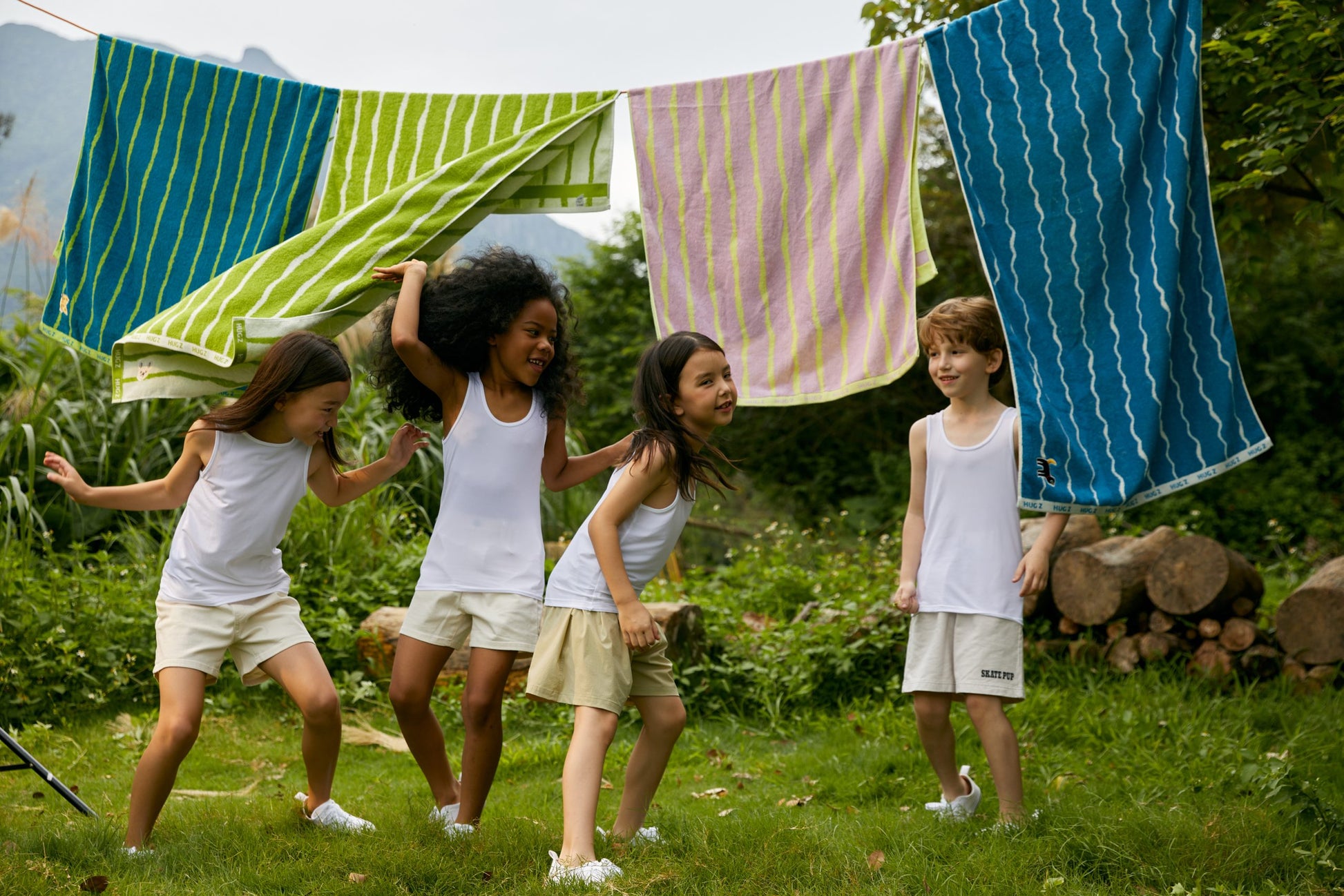 Dzieci bawiące się na trawie pod wiszącymi ręcznikami kąpielowymi dla dzieci marki HUGZ
