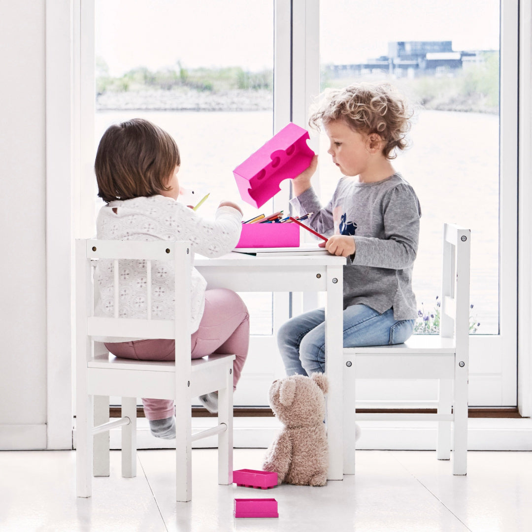 Dzieci bawiące się różowym lunchboxem klocek LEGO przy białym stoliku w jasnym pokoju