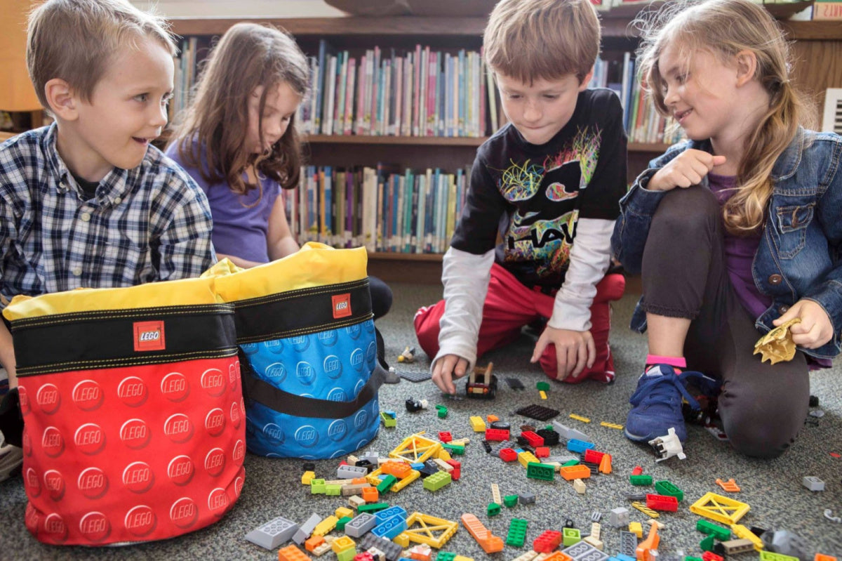 Dzieci bawiące się klockami LEGO obok kolorowych kubełków LEGO na klocki w pokoju z książkami