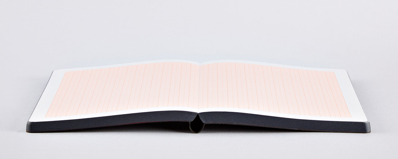 Otwarty notatnik w kratkę milimetrową z czerwonymi liniami i czarną okładką leżący na białym tle