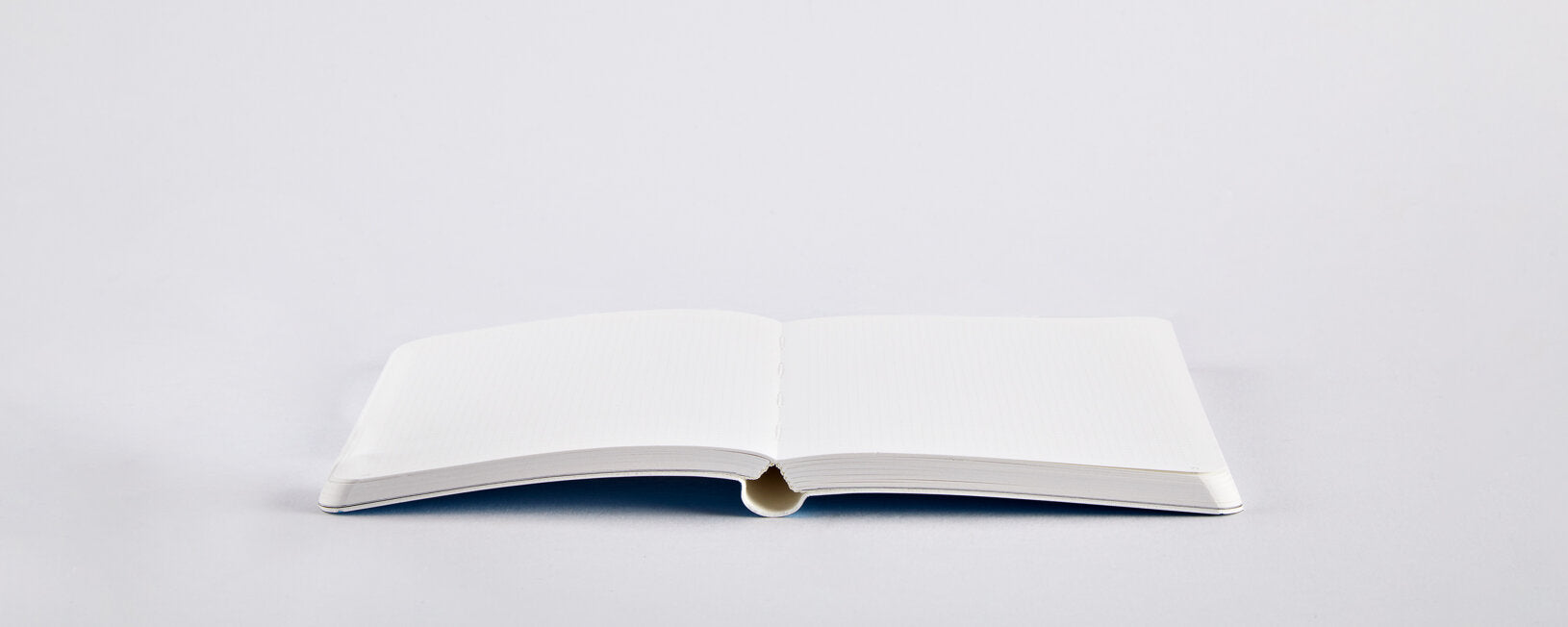 Otwarty notatnik Nuuna Pearl S niebieski z pustymi białymi stronami na szarym tle