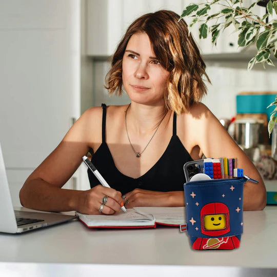 Czerwony piórnik LEGO czerwony astronauta z motywem kosmicznym na biurku obok kobiety piszącej notatki