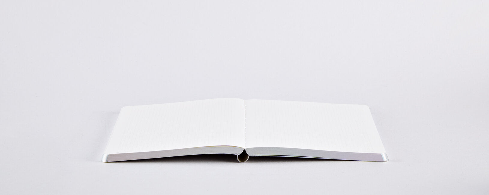 Otwarty notatnik Nuuna Fluid Chrome S z pustymi białymi kartkami na białym tle