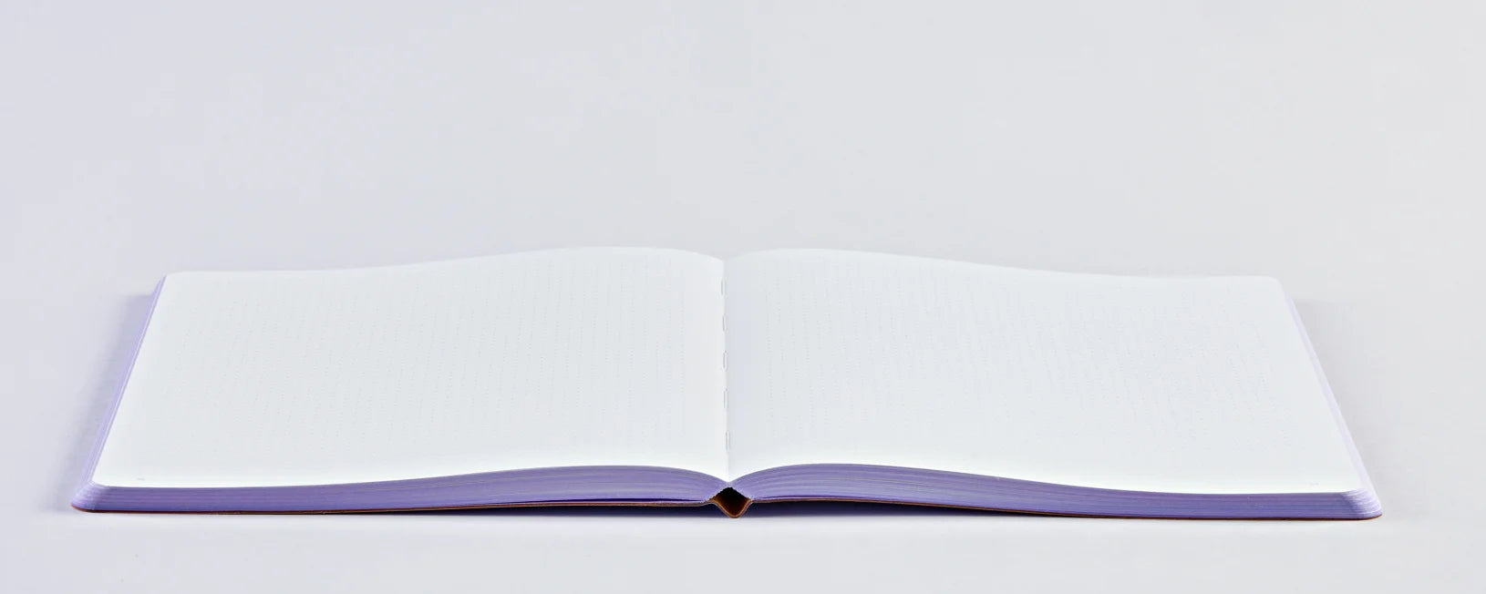 Notatnik fioletowy trance lilac otwarty na płasko z pustymi białymi stronami na jasnym tle