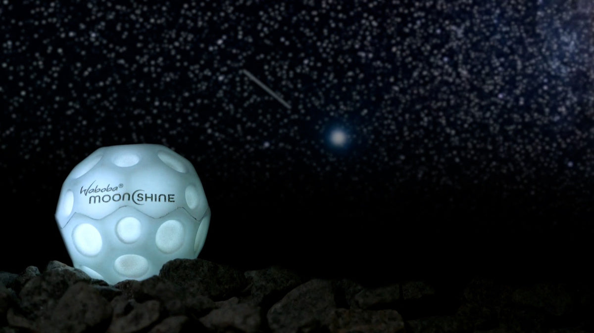 Piłeczka Waboba Moonshine odbijająca światło na tle gwiaździstego nieba i skał
