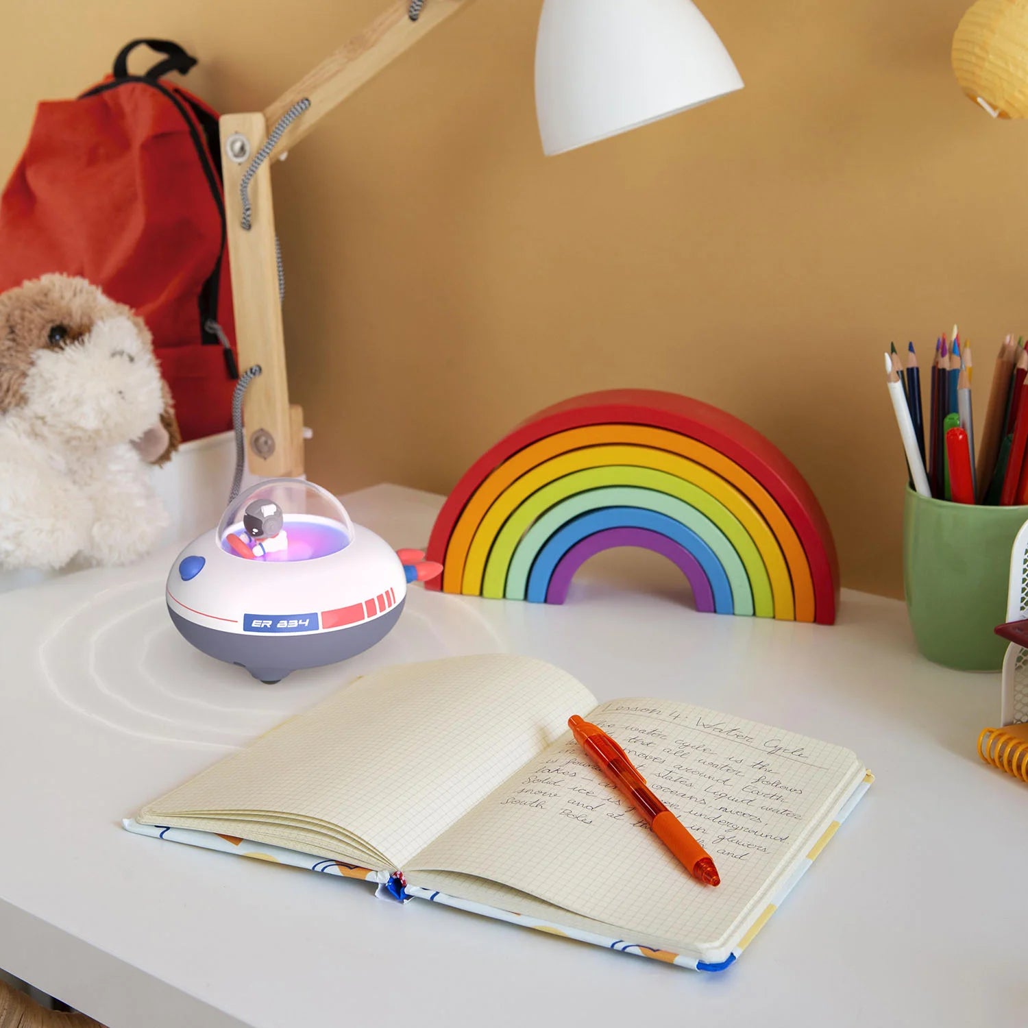 Świecący głośnik bezprzewodowy MOB na biurku obok notesu, tęczy i pluszowego misia