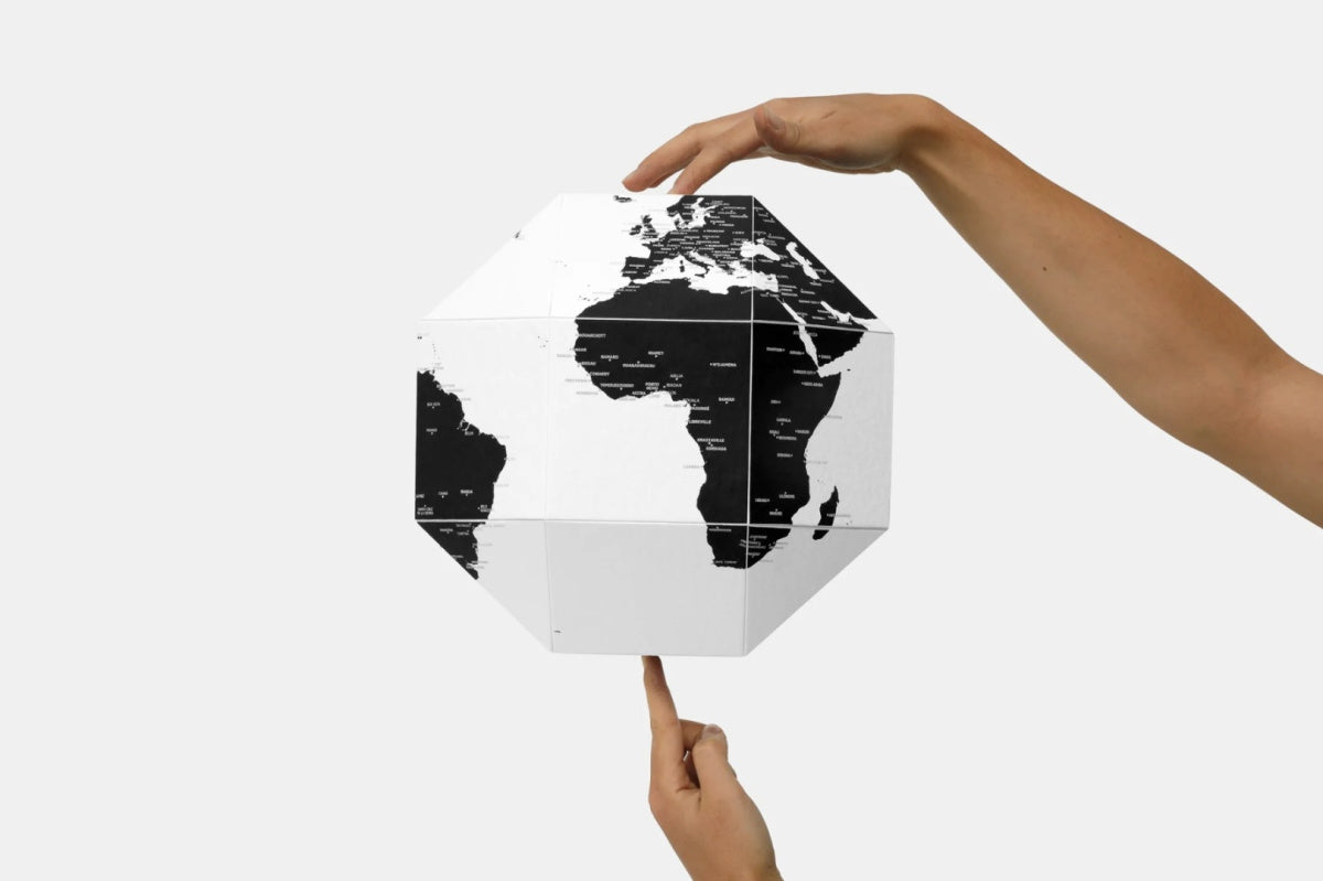 Biało-czarny globus z pinezkami trzymany w dłoniach na białym tle