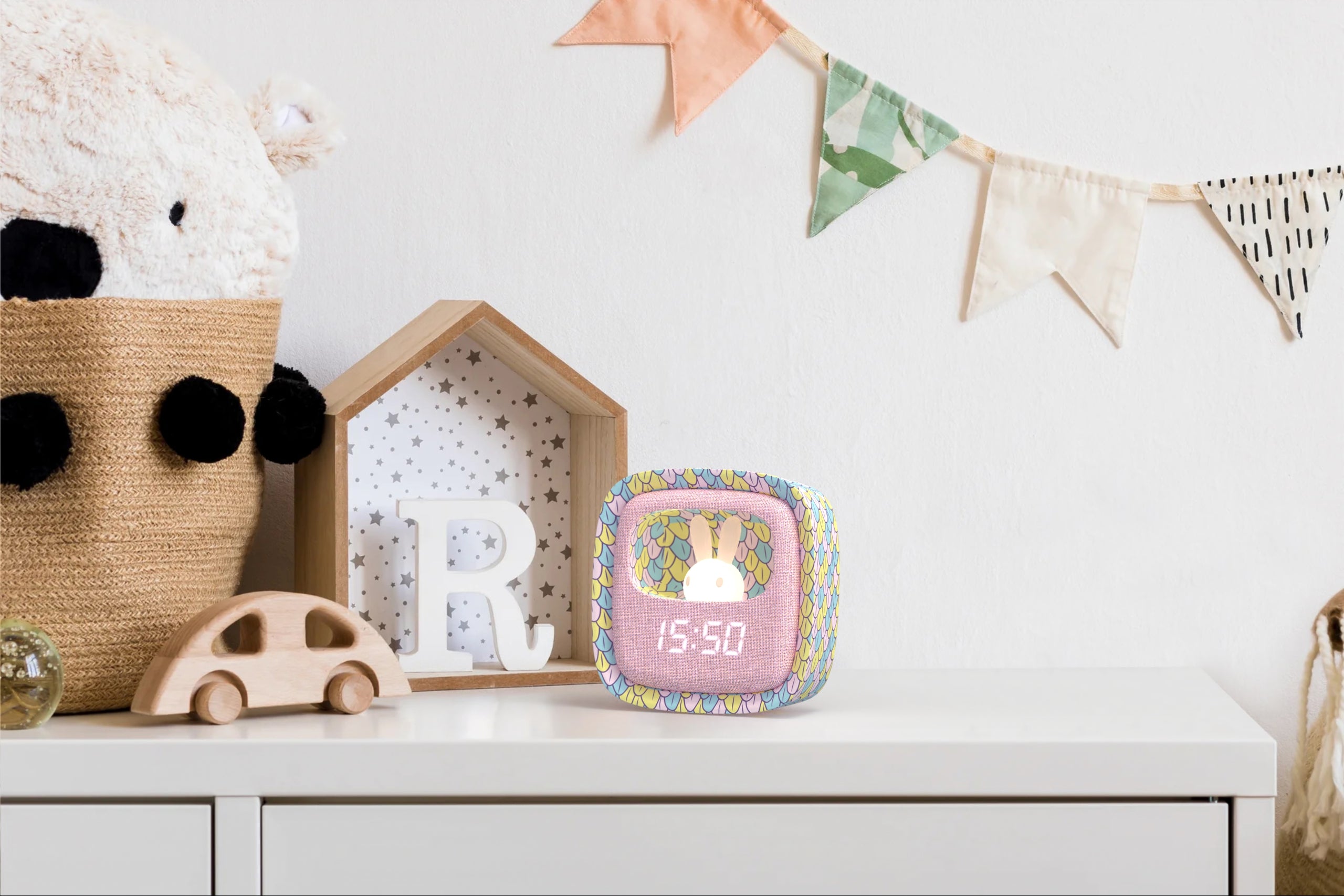 Kolorowy budzik dla dzieci z lampką pokazujący czas na białej półce w pokoju dziecięcym