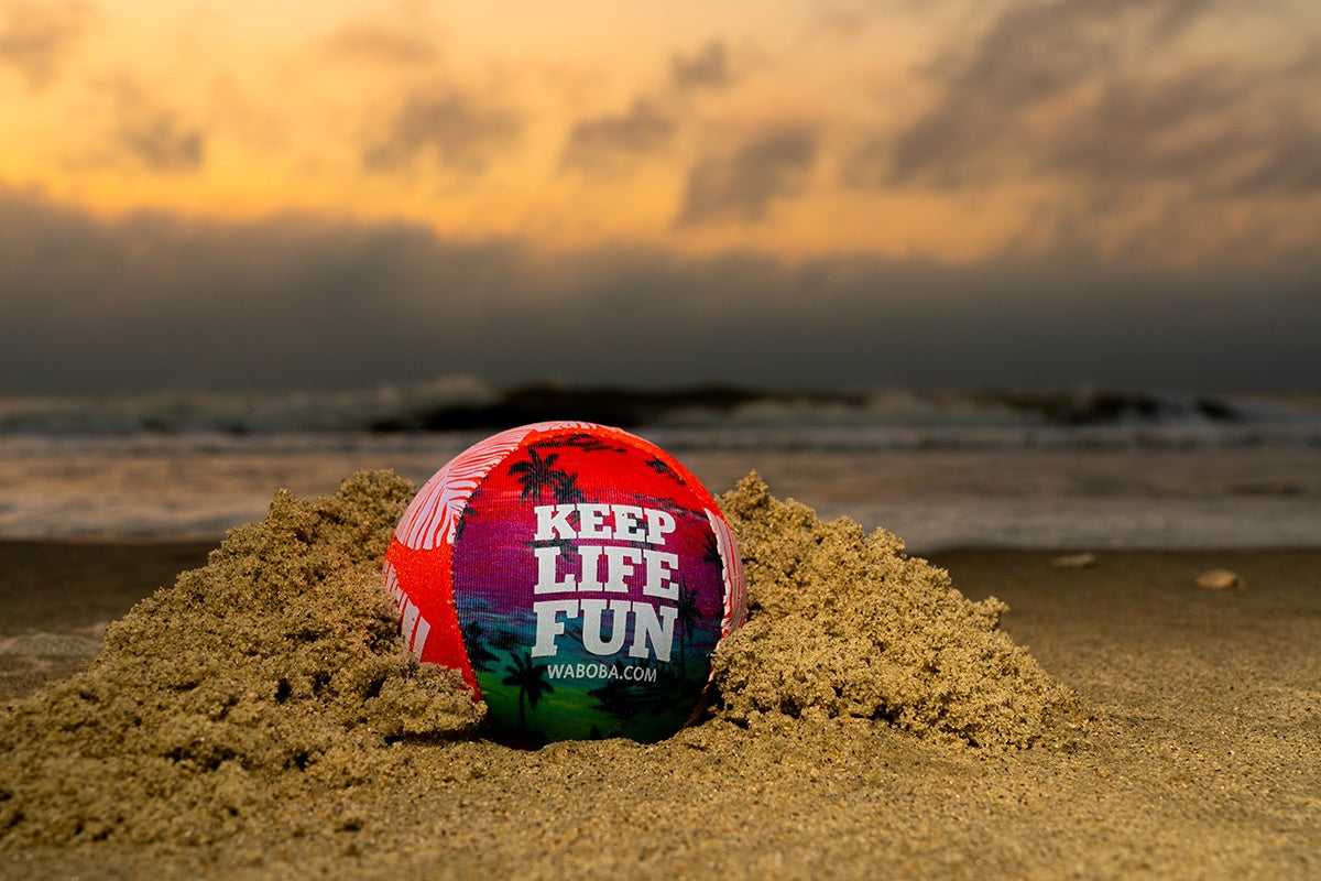 Kolorowa piłeczka Waboba Sol na plaży z napisem keep life fun przy zachodzie słońca