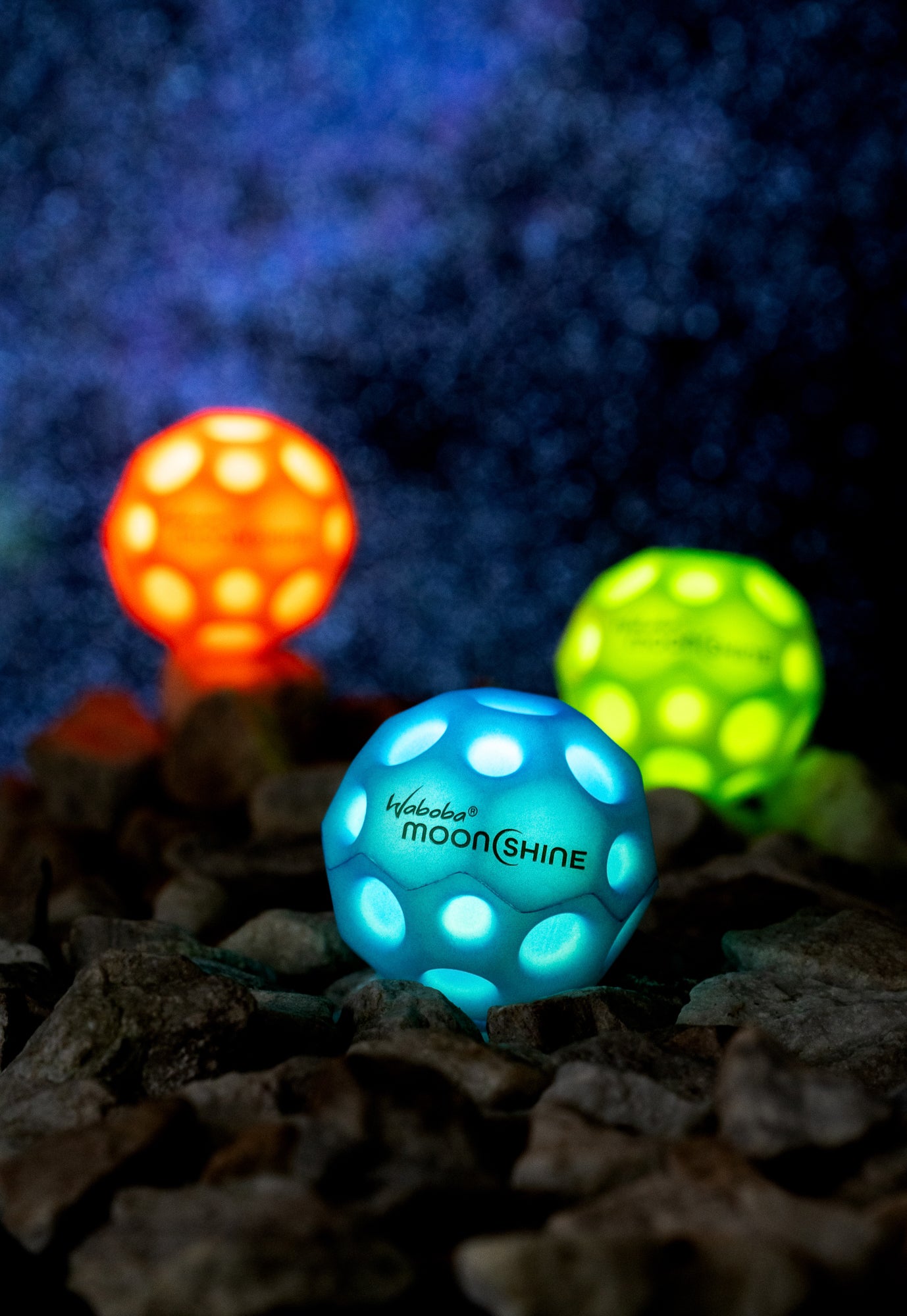 Niebieska piłeczka Waboba Moonshine niebieska świecąca na kamieniach w ciemnym otoczeniu