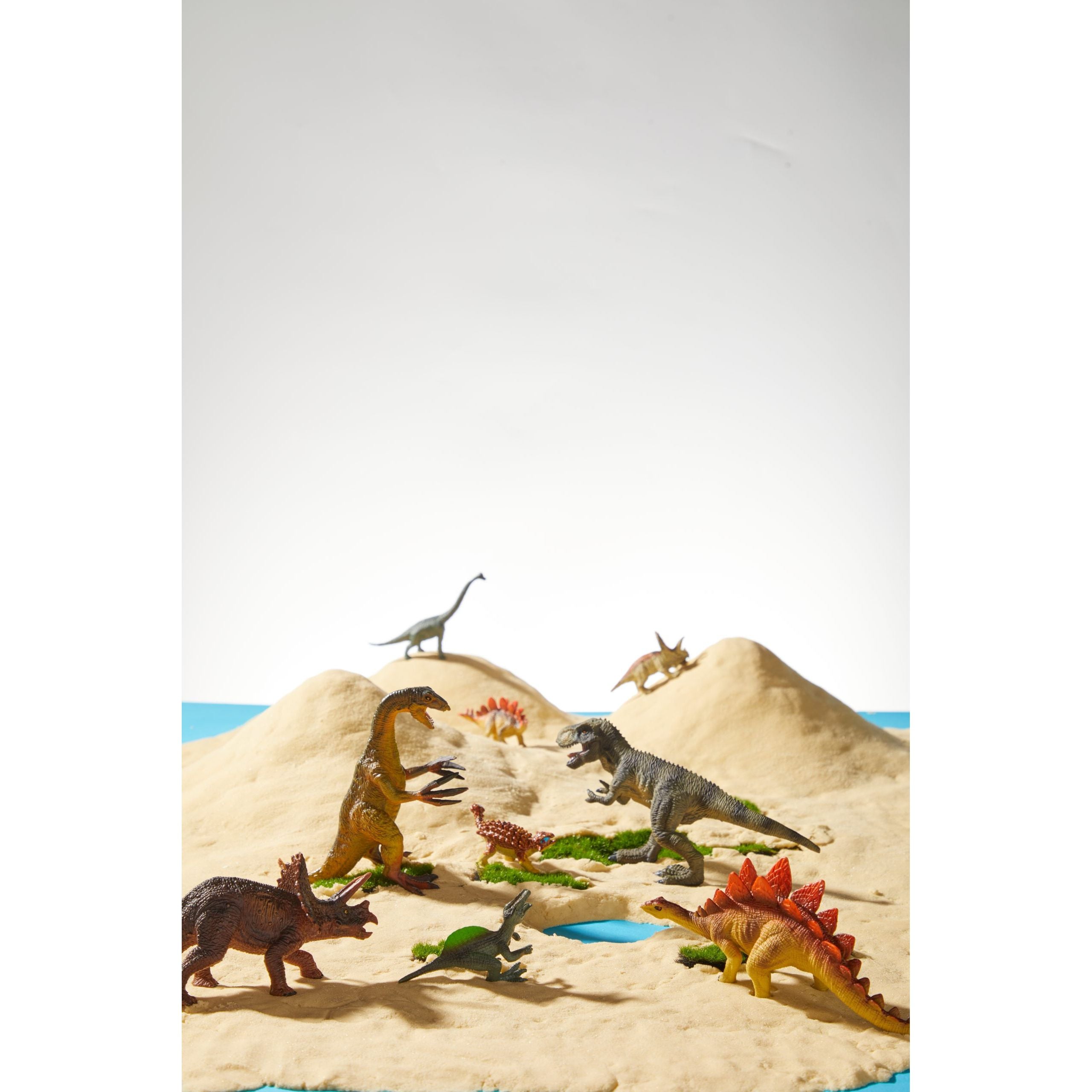 Zestaw figurek dinozaurów dla dzieci przedstawiający różne gatunki na piasku i zielonych liściach