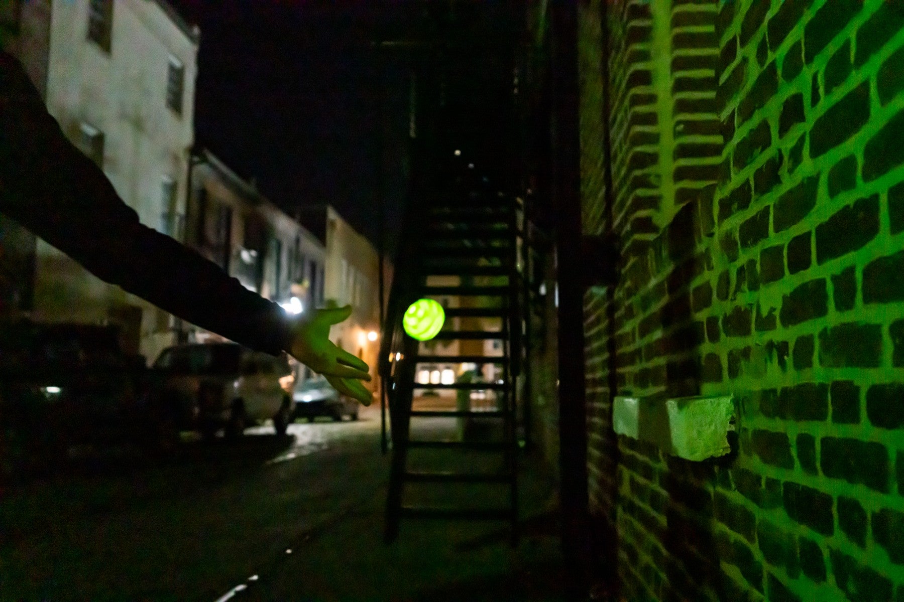 Osoba rzuca piłeczką świecąca Waboba Moonshine na nocnej ulicy przy ścianie budynku