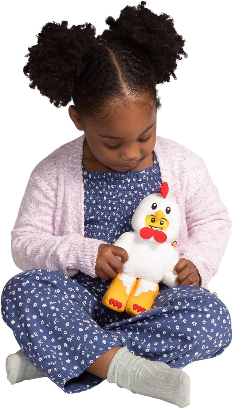 Dziecko trzymające pluszak LEGO kurczak w niebieskim kombinezonie i różowym sweterku
