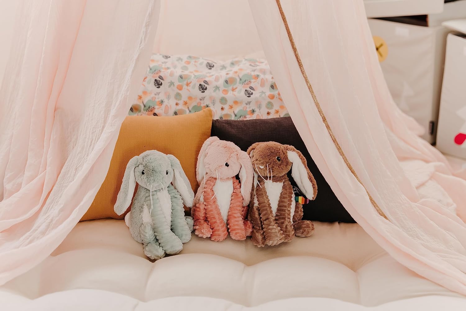 Pluszak królik różowy obok zielonego i brązowego pluszaka króliczka na łóżku z różowym baldachimem