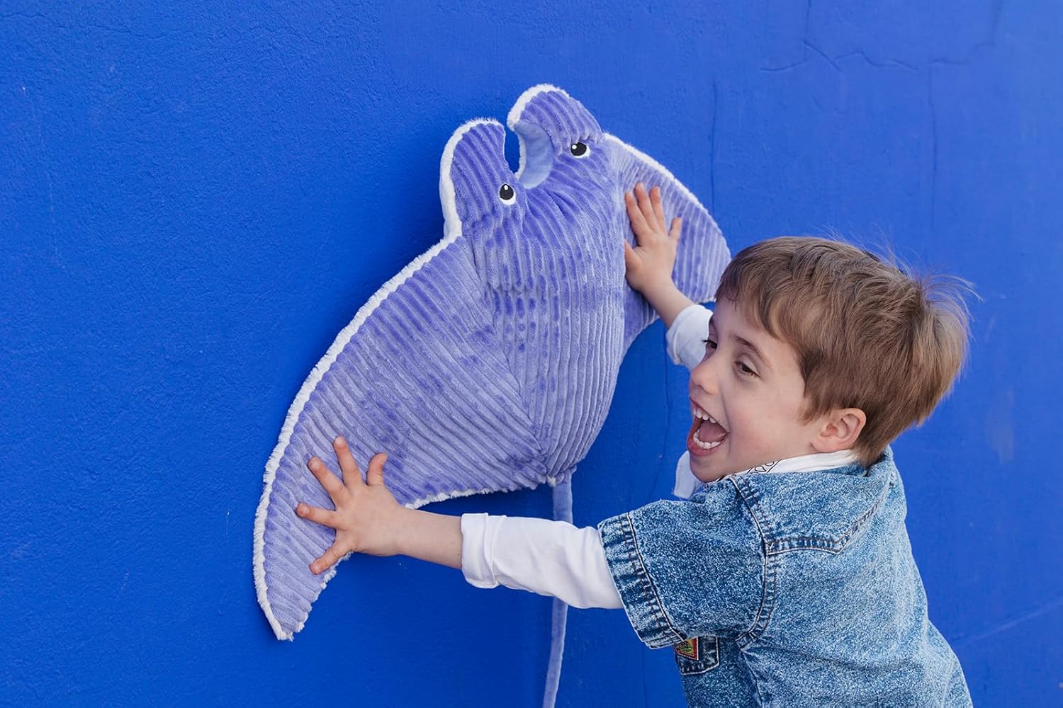 Pluszowa płaszczka fioletowa na ścianie z dzieckiem bawiącym się i dotykającym zabawki