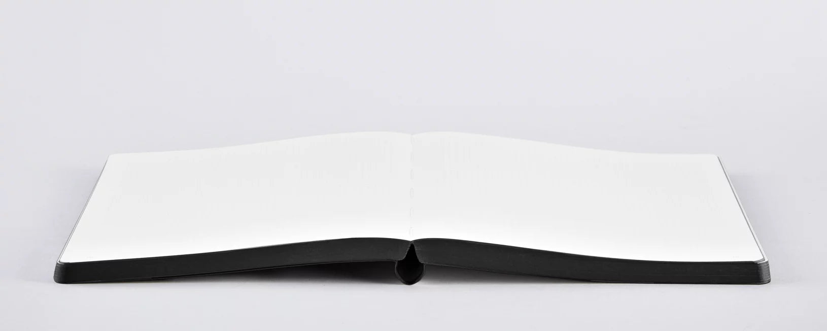 Notatnik Berlin otwarty z pustymi białymi stronami i czarną oprawą na płaskiej powierzchni